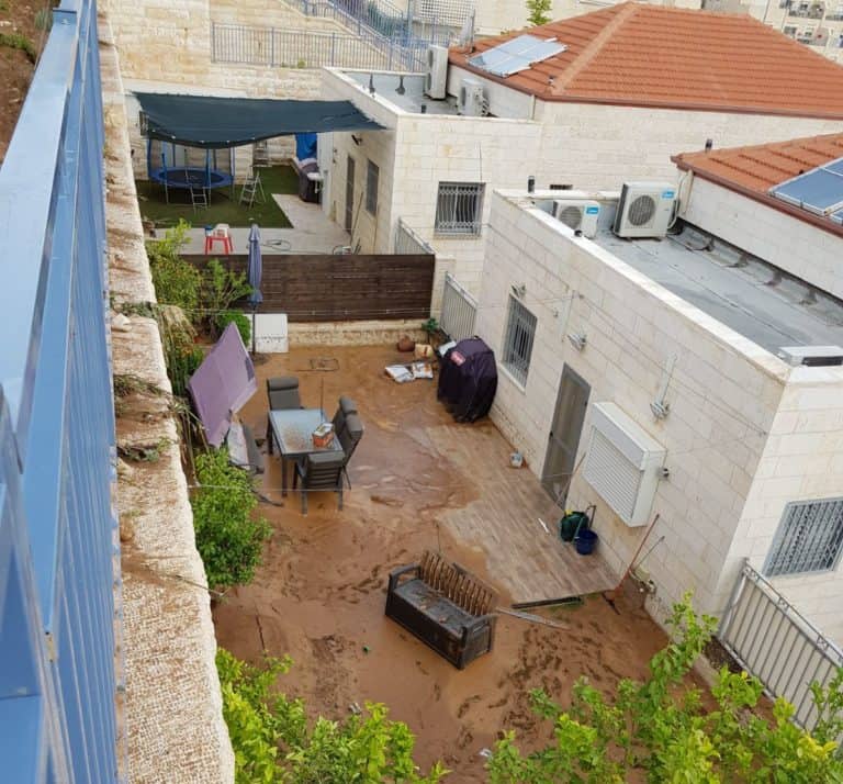 חצר מרוצפת של בית מוצפת במים עכורים, עד לקיר הבית וכיסאות הגן